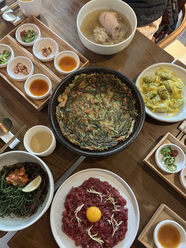 Wooden table full of different Korean foods on porcelain plates.