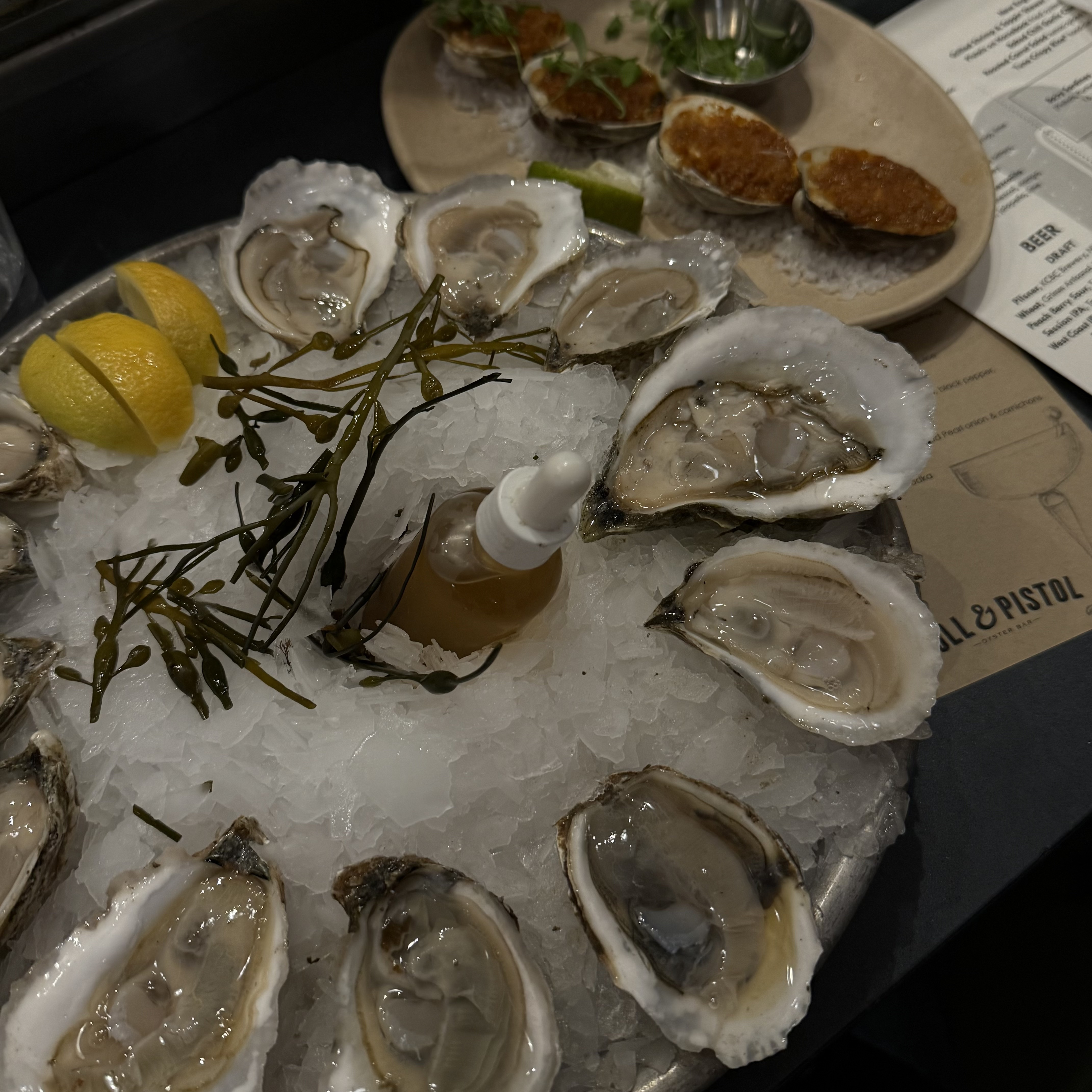 Raw oyster platter next to plate of seasoned raw mussels.