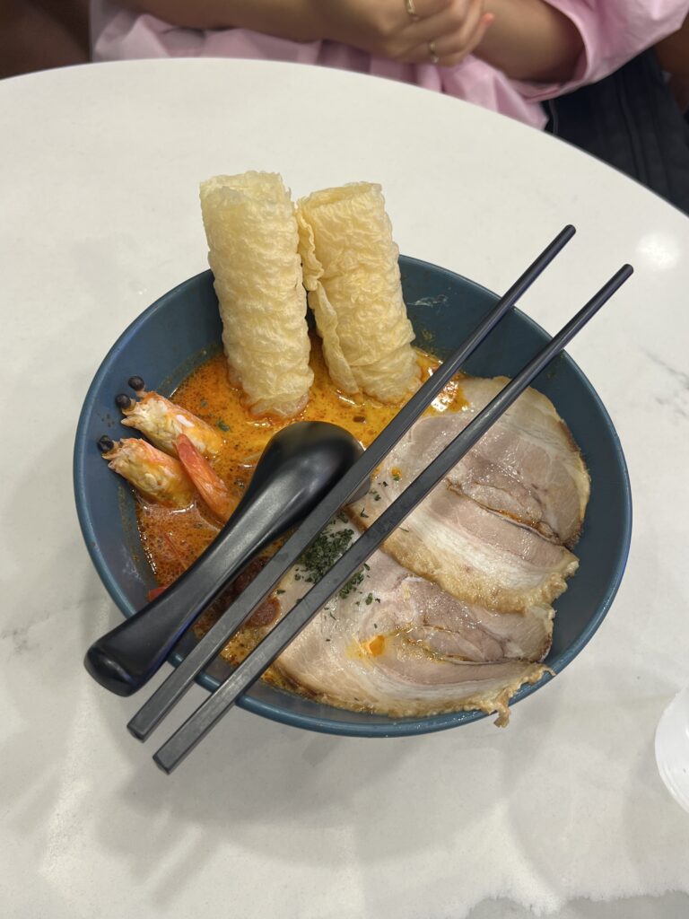 bowl of shrimp and pork singaporean laksa with utensils on top