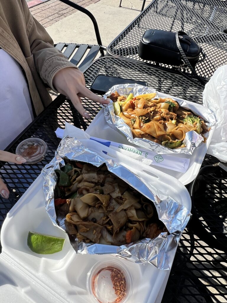 pad thai and pad see ew in takeout boxes on table outside